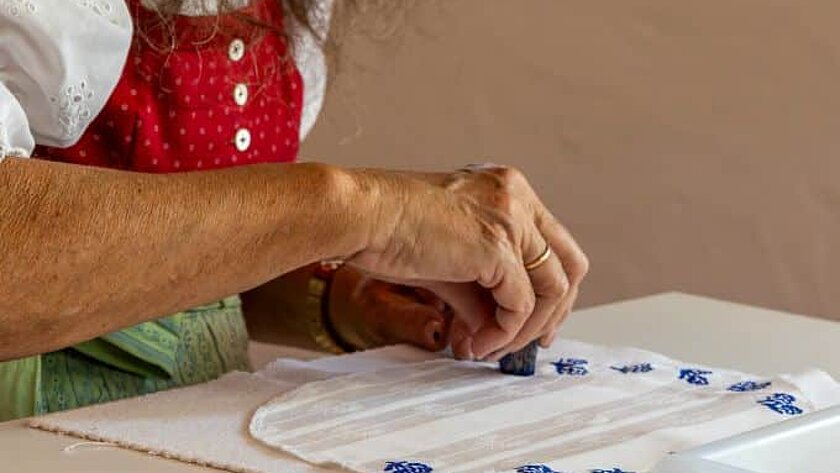 Eine Frau in Tracht stempelt auf Stoff.