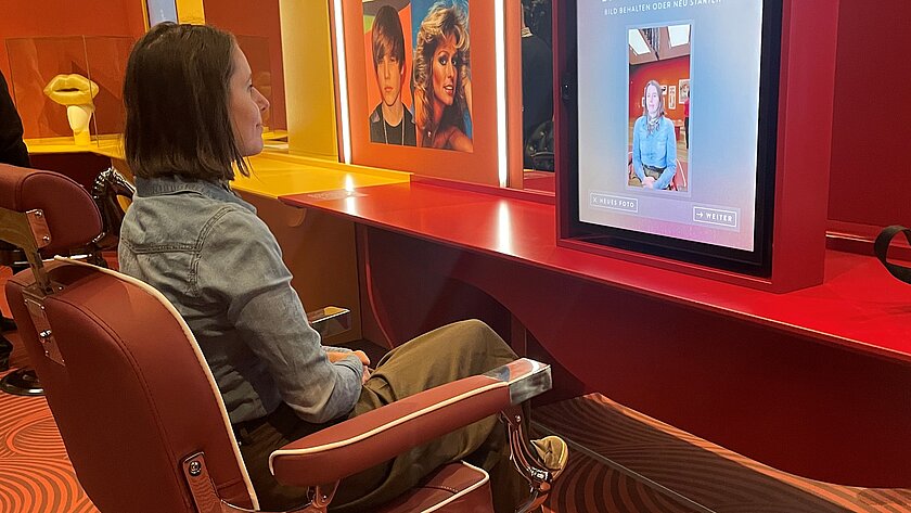 Frau, die auf einem Friseursessel in der Ausstellung sitzt